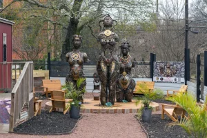 Three ornate sculptures on a raised platform surrounded by chairs and plants in an outdoor setting.