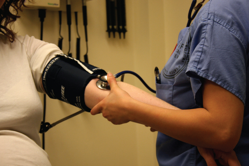 Healthcare professional taking a patient's blood pressure with a stethoscope and cuff.