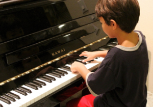 A young boy playing a black Kawai piano.