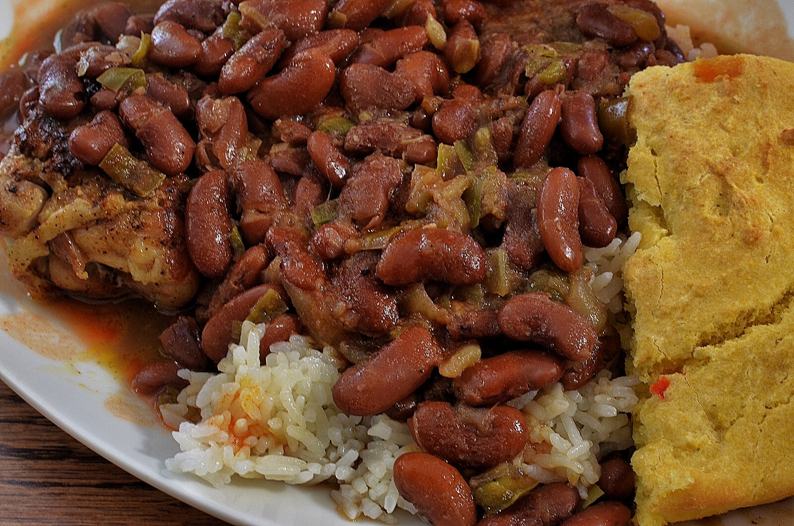 A plate of red kidney beans with green peppers over rice, accompanied by a slice of cornbread.