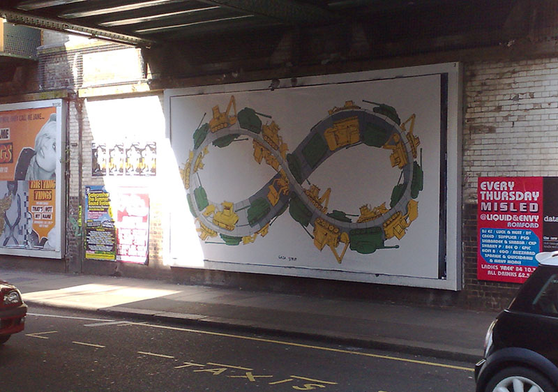 Street underpass with a large billboard showing an infinity loop of bulldozers and dump trucks; other posters and “TAXIS” road marking. (Image Description available)