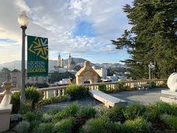 Hilltop campus terrace overlooking a city skyline and church spires, with green banner and gardens.